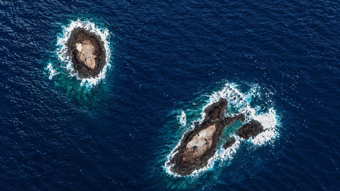 Vista aérea das duas formações rochosas das Ilhas Rasas em Guarapari, ponto de mergulho com águas mais claras e fauna marinha de grande porte da costa capixaba
